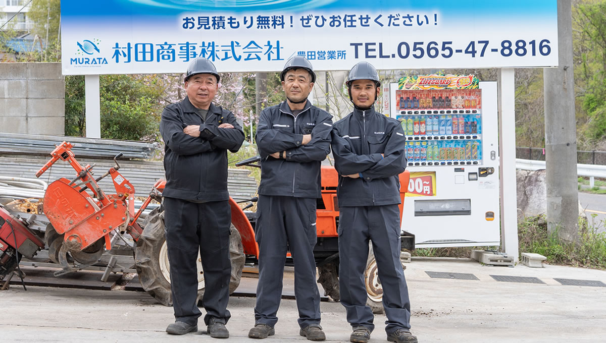 鉄・金属の買取をPRする豊田営業所の作業員3名が看板の前に立っている
